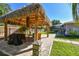 Tiki hut with a grill overlooking the paved path to screened pool and lush landscaping in the backyard at 143 58Th S Ave, St Petersburg, FL 33705