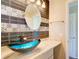 Bathroom vanity with a blue glass bowl sink, designer tile backsplash, and oval mirror at 7509 Mesa St, North Port, FL 34287