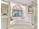 Bright bathroom featuring soaking tub, glass enclosed shower, and arched window with decorative shade at 8823 Crescent Forest Blvd, New Port Richey, FL 34654