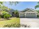 Charming gray home showcasing a three-car garage, tiled roof, well-manicured lawn and tropical landscaping at 9302 Deer Creek Dr, Tampa, FL 33647