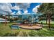 Community playground with shade covering, surrounded by manicured lawn, shrubbery and trees, plus play equipment at 15925 Pond Rush Ct, Land O Lakes, FL 34638