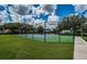 View of the community tennis court surrounded by tall fence, green grass and residential homes at 15925 Pond Rush Ct, Land O Lakes, FL 34638