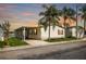 Charming single-story home with carport, lush lawn, and mature palm trees set against a colorful sunset sky at 8632 Fantasia Park Way, Riverview, FL 33578