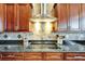 Close-up of the kitchen with stainless steel hood and cooktop with dark countertops and custom tile backsplash at 1408 Alhambra Dr, Apollo Beach, FL 33572