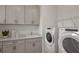 Bright laundry room features cabinetry, a sink, modern washer and dryer appliances, and a wire rack for optimal organization at 9825 Autumn Ridge Ave, Riverview, FL 33578