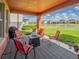 Covered patio with outdoor seating, a fire pit, a grill, and serene views of the pond and well-manicured backyard at 28923 Lucero Ln, Wesley Chapel, FL 33543
