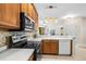 Kitchen with wooden cabinetry, tile backsplash, modern appliances, and a view of living area at 1922 Sifield Greens Way # 47, Sun City Center, FL 33573