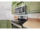 Modern kitchen featuring stainless steel microwave, range, green cabinets and countertops at 5745 Pawnee St, Zephyrhills, FL 33542