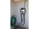 Close-up of a wall-mounted AUTEL electric car charger with a coiled green garden hose nearby at 11233 51St N Ave, St Petersburg, FL 33708