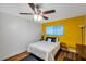 Cozy bedroom with a yellow accent wall, wood floors, and a comfortable bed complemented by a modern ceiling fan at 1801 Bedford Ter # 221, Sun City Center, FL 33573