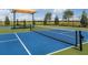 Outdoor tennis court with blue and green surface, shaded seating area, and black net against a sunny sky at 6338 Springline Pl, Apollo Beach, FL 33572