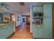 An open kitchen showcasing stainless appliances, green cabinetry with granite counters and wood-look tile flowing through the home at 1439 Wetherington Way, Palm Harbor, FL 34683