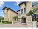 Close-up of a Mediterranean-style home featuring arched windows, stucco walls, and lush palm trees against a blue sky at 17005 Madres De Avila, Tampa, FL 33613