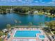 Aerial view featuring a sparkling blue pool, surrounded by palm trees and lush greenery, and overlooking a serene lake at 1333 Shady Pine Way # F, Tarpon Springs, FL 34688