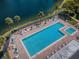 Aerial view of a pool with lounge chairs, umbrellas, and palm trees alongside a tranquil lake at 1333 Shady Pine Way # F, Tarpon Springs, FL 34688