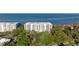 Aerial view of a white mid-rise condominium building surrounded by lush greenery and blue ocean waters at 2410 Harbourside Dr # 142, Longboat Key, FL 34228
