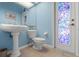 Charming blue bathroom featuring a pedestal sink, toilet, and a stained glass door, creating a tranquil space at 16340 Marquis Rd, Brooksville, FL 34614