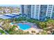 An aerial view of the in-ground pool with lounge chairs, tiki huts, and a backdrop of lush greenery at 400 Island Way # 1708, Clearwater Beach, FL 33767