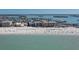 Aerial view of a sandy beach with people, blue umbrellas, and calm ocean waters near beachfront condominiums at 12924 Gulf Blvd # 502, Madeira Beach, FL 33708