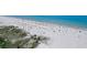Aerial view of a sandy beach with calm, clear ocean water and scattered beach umbrellas at 121 46Th Ave # 2H, St Pete Beach, FL 33706