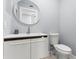 Modern powder room featuring sleek white vanity, round mirror and toilet at 7049 Peninsular Dr, New Port Richey, FL 34652