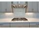 Modern stovetop with stainless steel range hood and white backsplash with gray accents against light gray cabinets at 14239 Swiss Bridge Dr, Riverview, FL 33579