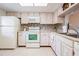 Bright kitchen featuring white cabinetry and appliances, tiled backsplash, and a window offering views of adjacent spaces at 3610 Magnolia Ridge Cir # 1322/H, Palm Harbor, FL 34684