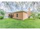 A green backyard with the home's tan exterior featuring a chimney and trimmed foliage at 2706 Bent Leaf Dr, Valrico, FL 33594