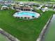 Aerial view of the community pool with a unique shape, surrounded by palm trees, with green space at 7737 Sail Clover Ln, Zephyrhills, FL 33540