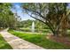 Scenic pond featuring a central fountain, surrounded by lush trees, a sidewalk, and a manicured lawn at 1187 Mistwood Dr, Tarpon Springs, FL 34688