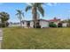 Lawn of home with lush green grass, palm trees, a white fence, and view of covered patio at 11755 7Th E St, Treasure Island, FL 33706