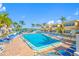 Community pool with many lounge chairs surrounded by palm trees with yellow buildings at 19417 Gulf Blvd # B-210, Indian Shores, FL 33785