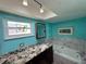 Bright bathroom with stylish granite vanity, a window, bathtub with custom tile, and contemporary fixtures at 6319 Cocoa Ln, Apollo Beach, FL 33572