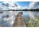 Wooden dock stretching into a serene lake, reflecting the cloudy blue sky and surrounding trees at 3207 Lake Padgett Dr, Land O Lakes, FL 34639
