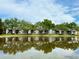 Waterfront two-story condo building reflected in a pond with mature trees and blue skies at 3821 N Oak Dr # J31, Tampa, FL 33611