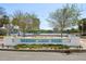 The Mirror Lake Park sign sits between two trees with the lake and city buildings in the background at 701 Mirror Lake N Dr # 119, St Petersburg, FL 33701