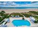 Aerial view of a pool with lounge chairs and umbrellas surrounded by greenery overlooking the beach at 1350 Gulf Blvd # 502, Clearwater Beach, FL 33767