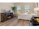 Bright bedroom features wood floors, a white bed, television, and a large houseplant near the windows at 4839 Pointe O Woods Dr, Wesley Chapel, FL 33543