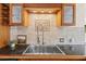 Close-up of a stainless steel sink with granite countertops and wooden cabinets with stone backsplash at 301 71St S St, St Petersburg, FL 33707
