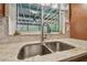 Close-up of a kitchen sink with stainless steel faucet and marble countertops, with view to the enclosed patio at 4555 Debbie Ln, Lutz, FL 33559