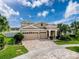 Attractive home showcasing a three-car garage, lush landscaping, and a brick-paved driveway at 8578 Gibbons Grove Loop, Land O Lakes, FL 34637