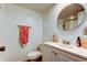 Well-lit bathroom with white vanity, round mirror, and decorative coral-themed hand towel at 225 Country Club Dr # 1104, Largo, FL 33771