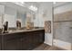 Bathroom with dual sinks, granite countertops, dark cabinetry, and a tiled walk-in shower at 18185 Cortes Creek Blvd, Spring Hill, FL 34610