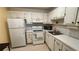 View of the kitchen features white cabinets and a suite of white appliances and lots of counter space at 1801 Bedford Ln # 46, Sun City Center, FL 33573