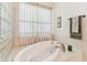 Spa bath with large tub, glass block partition, tile surround, and window with light-filtering curtains at 18502 Keystone Manor Rd, Odessa, FL 33556