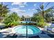 A hot tub is surrounded by tropical foliage, palm trees, and a pool with a clubhouse in the background at 12408 Palatka Dr, Venice, FL 34293