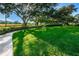 A walkway leads to a lush green lawn surrounded by mature trees and manicured hedges at 36750 Us 19 N Hwy # 18-210, Palm Harbor, FL 34684