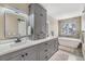 Modern bathroom featuring double sinks, grey cabinets, and a soaking tub next to a window at 9481 Highland Oak Drive # 602, Tampa, FL 33647