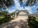 Beautiful exterior showcasing a two-car garage, brick-paved driveway, and vibrant tropical foliage at 9980 Sago Point Dr, Seminole, FL 33777