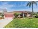 Charming single-story home featuring a beautiful lawn, colorful landscaping, and a welcoming pink garage door at 3136 Sandhill Dr, Holiday, FL 34691